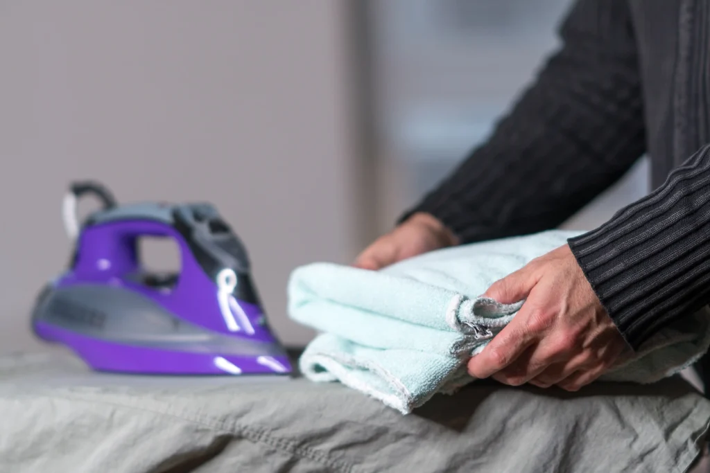 midsection-man-folding-towel-ironing-board
