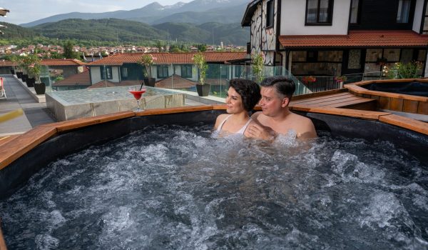 Двама гости се наслаждават на минерална вода в открита дървена вана в Ruskovets Thermal SPA & Ski Resort