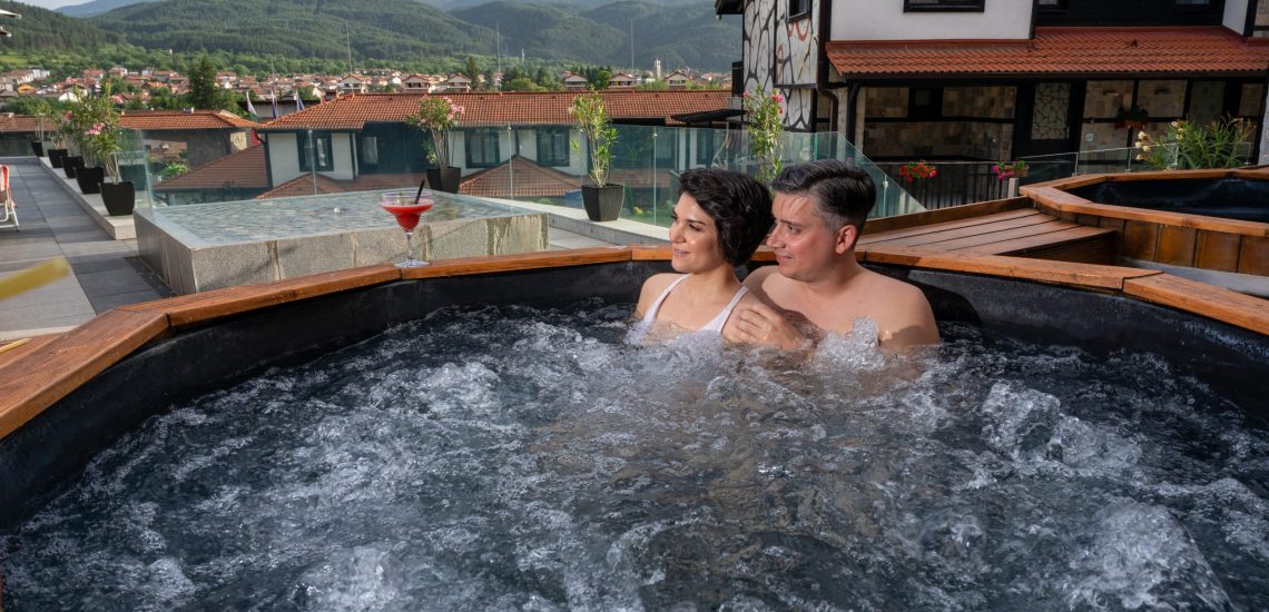 Двама гости се наслаждават на минерална вода в открита дървена вана в Ruskovets Thermal SPA & Ski Resort